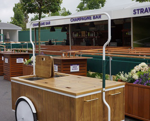A wooden food cart with a bent metal tube arched over the top